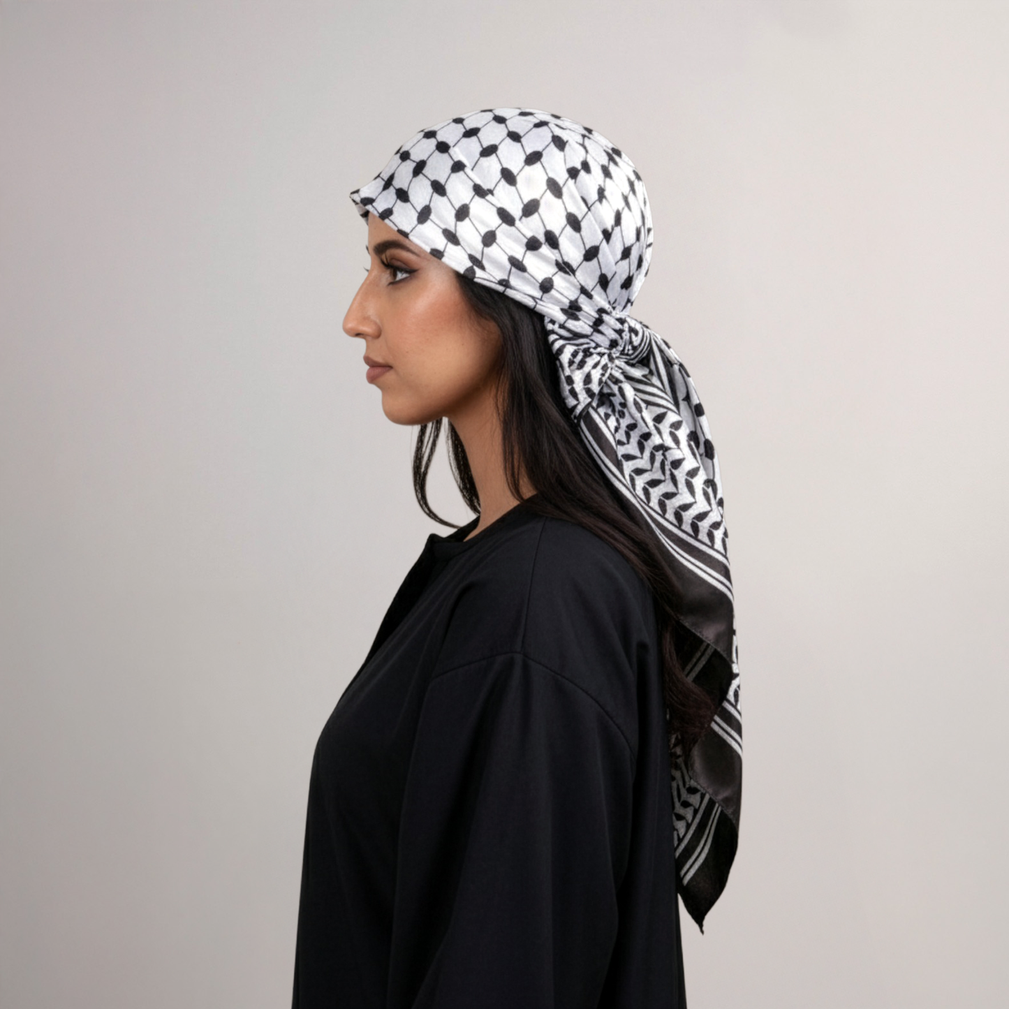 Woman wearing a black and white patterned headscarf on a plain background